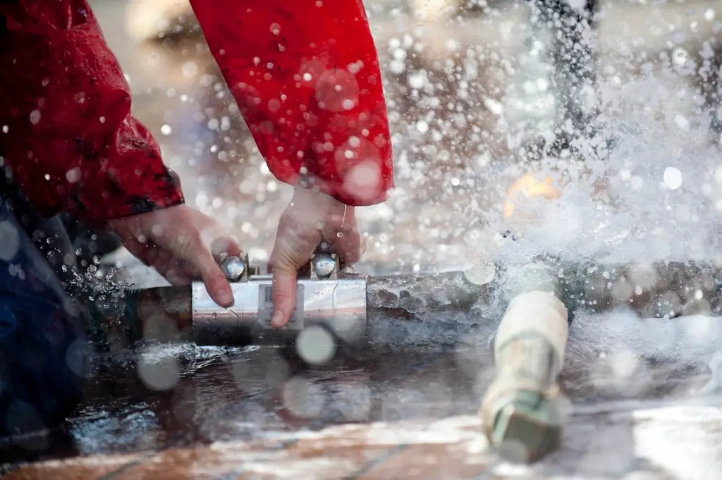 Hands working on a pipe fitting as water sprays from a leak